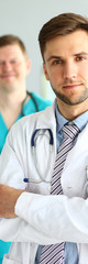 Portrait of handsome man in white uniform with stethoscope. Smiling doc posing at workplace in clinic office. Medical treatment concept. Blurred background