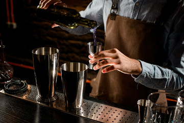 Male bartender pouring a alcoholic drink from the bottle to a steel jigger