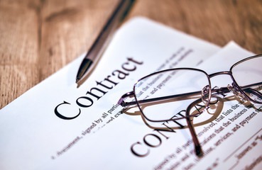 Contract sheet with glasses and a pen on a wooden background