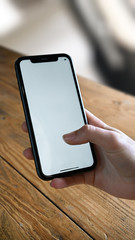 Woman with smartphone with empty screen in front of a wooden table at home. 