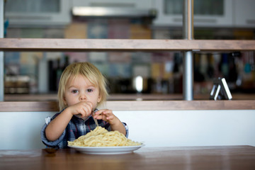 Little baby boy, toddler child, eating spaghetti for lunch and making feeding teddy bear friend