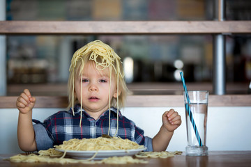 Little baby boy, toddler child, eating spaghetti for lunch and making feeding teddy bear friend