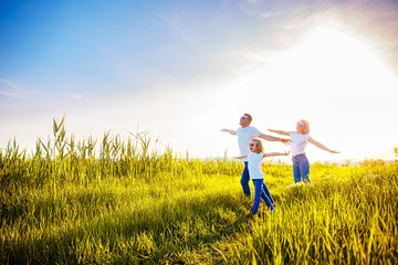 Photo A happy family in white T-shirts, sunglasses and jeans in the park spread apart arms mimicking airplanes. Summer. Vacation air travel concept.