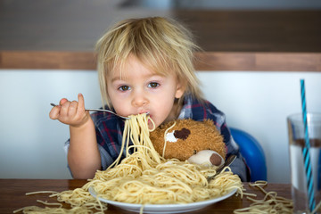 Little baby boy, toddler child, eating spaghetti for lunch and making feeding teddy bear friend