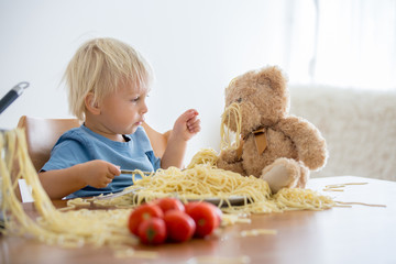 Little baby boy, toddler child, eating spaghetti for lunch and making feeding teddy bear friend