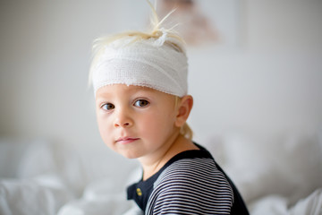 Close portrait of little toddler boy with head injury, sitting in bed, tired
