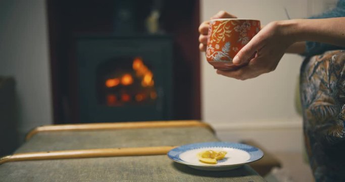 Young woman drinkng tea and eating cake by log burner