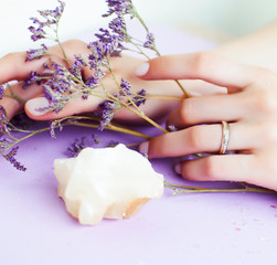 pretty perfect woman hands with white manicure and little flowers on colorful lilac background, green leaf spa concept