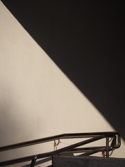 A white wall with a handrail, light divides the wall in half into a shadow