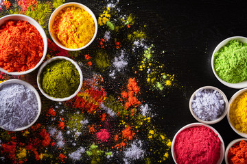 Holi festival celebration. Traditional Indian Holi colours powder decoration with paints. Top view of Organic Gulal colors in bowls, spices, rustic on black background for Holi festival.