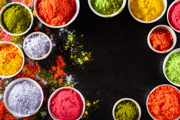 Holi festival celebration. Traditional Indian Holi colours powder decoration with paints. Top view of Organic Gulal colors in bowls, spices, rustic on black background for Holi festival.