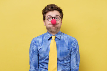 Young handsome man with red clown nose blowing cheeks.