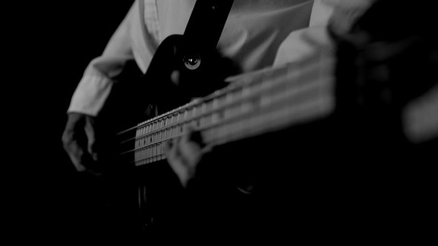ECU ON A BASS PLAYER'S HANDS PLAYING AN OPEN "E" STRING.  IN BLACK AND WHITE.  FHD.