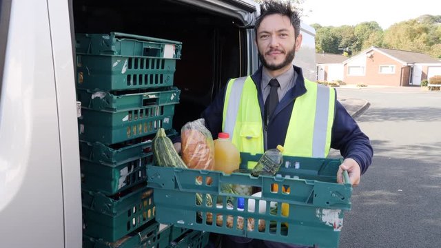 Smiling delivery man holds crate of groceries next to van