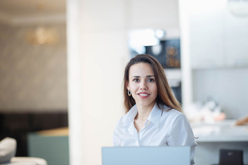 young Caucasian woman in a modern office is working behind a white laptop in business clothes.