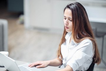 young Caucasian woman in a modern office is working behind a white laptop in business clothes.