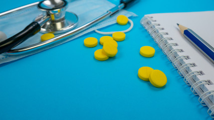Yellow Pharmaceutical Medicine Pills. Stethoscope and Face Mask on Blue Background. Pencil and Paper Notebook in hospital. Concept of health care, nurse or doctor, clinic or hospital