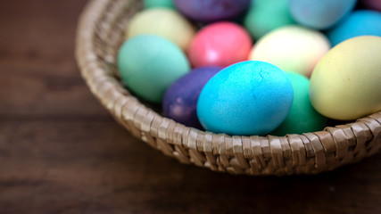 Fototapeta na wymiar Easter background - Basket filled with colored Easter eggs on a rustic wooden table