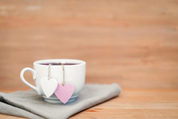 Heart shaped tea bag in white cup of tea - cute love declaration on wooden background, selective focus. Valentines day concept. Mug of tea for two lovers honeymoon wedding morning surprise breakfast