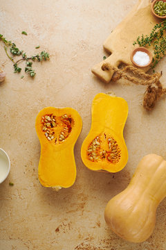 Halved butternut squash with cream, thyme and garlic on beige background. Ingredients for cooking dinner. Flatlay.