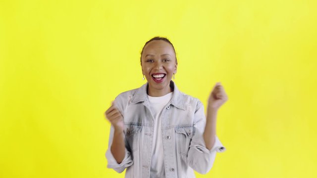 Beautiful happy african young woman saying OH MY GOD and dancing on yellow background Jean jacket