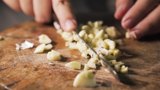 chef cutting peeled garlic on top of a wooden board. from out to in focus. slow motion.
