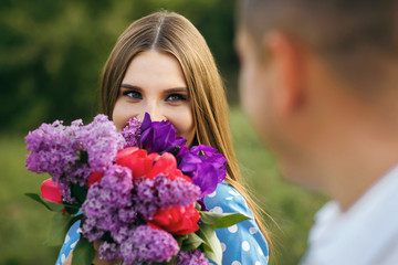 A girl with beautiful eyes holds a bouquet of spring flowers and looks at her boyfriend