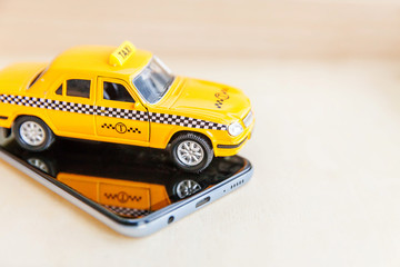 Smartphone application of taxi service for online searching calling and booking cab concept. Simply design yellow toy car Taxi Cab on empty screen of smart phone on wooden background. Taxi symbol.