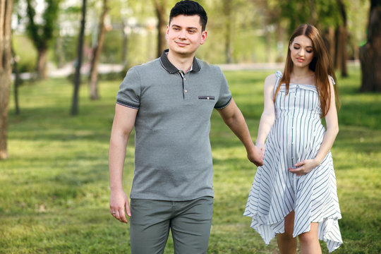 Young expectant mother and her boyfriend are walking in the park, husband and wife are walking in the fresh air waiting for the child
