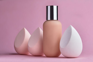 Conatainer with fluid foundation with beauty blender.Cosmetic branding, glamour and skincare concept - Tonal bb cream bottle make-up fluid foundation base for nude skin color on pink background