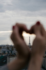 The Eiffel Tower in the urban space of the daytime city through hands folded in the form of a heart. The view from the roof of the houses.