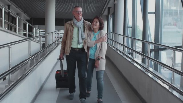Beautiful senior couple walking in the hallway of airport with luggage and hugging