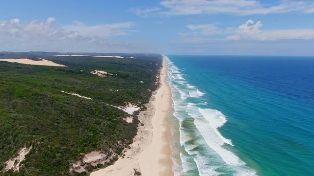 High angle aerial drone footage of famous Seventy Five Mile Beach on Fraser Island, Queensland, Australia. The Island is popular for tourist with four-wheel drive vehicles. Sand blows on the left.