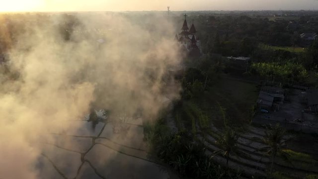 Bali, Indonesia - A Beautiful Scenery Of Rice Field Plantation With View Of Jemaat Marga Pakerti Church With A Dramatic Smoky Effect At Sunrise - Aerial Shot