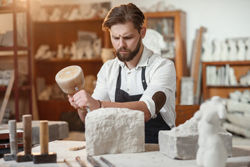 Stone carver works with wooden hammer and chisel at limestone. - obrazy, fototapety, plakaty