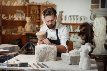 Stone carver works with wooden hammer and chisel at limestone.