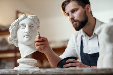 Skillful sculptor makes professional restauration of gypsum sculpture of woman's head at the creative workshop.