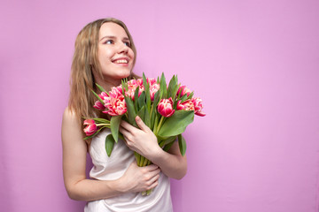 girl holds and sniffs a bouquet of flowers on a pink background, a beautiful woman with tulips
