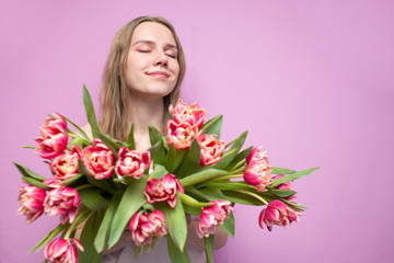 young beautiful girl holds a bouquet of flowers on a pink background, happy woman with tulips dreams,
