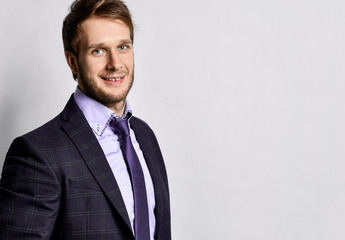 Young positive handsome man in official costume and tie standing over light grey wall background