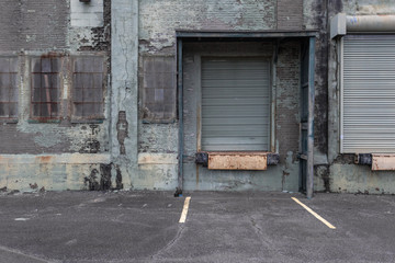 Back of a vintage industrial building with faded green paint and closed loading dock