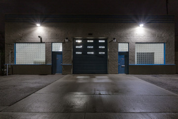 Two blue doors and a large garage door on the back of an industrial building at night with star burst lights - obrazy, fototapety, plakaty