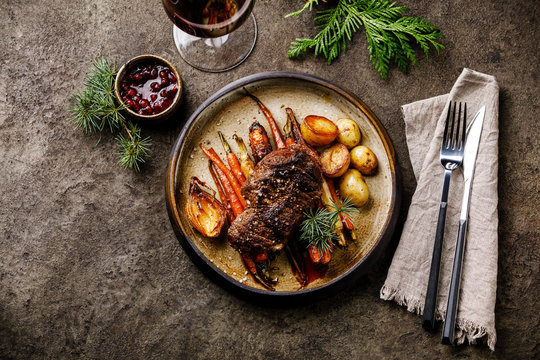 Grilled Venison Steak with baked vegetables and berry sauce and Red wine on dark background