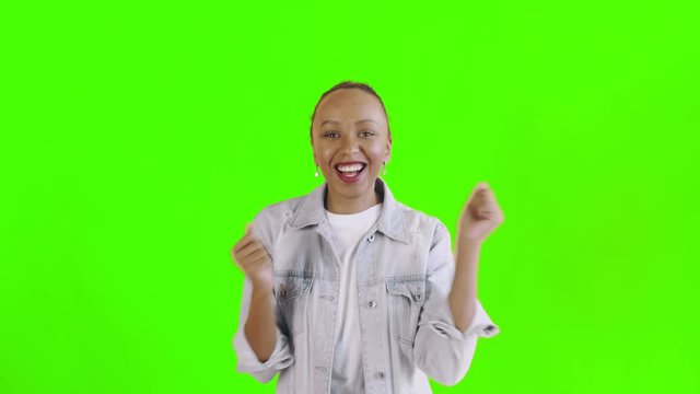 Beautiful happy african young woman saying OH MY GOD and dancing on green background Jean jacket