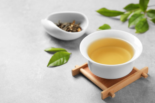 Cup of green tea, dry and fresh leaves on grey table. Space for text