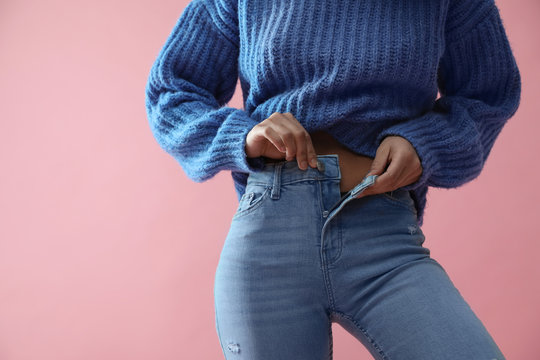 Woman unbuttoning jeans on pink background, closeup