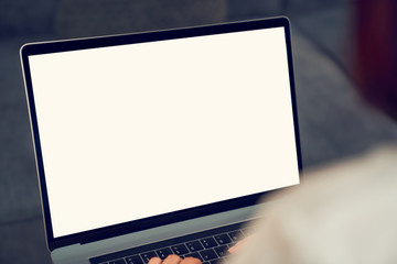 Woman hand using laptop on sofa in house, mock up of blank screen.