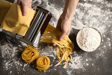 Woman preparing noodles with pasta maker machine at grey table, top view - obrazy, fototapety, plakaty