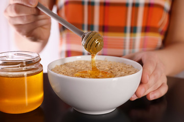Woman adding honey to oatmeal at black table, closeup