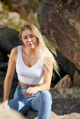 Obraz premium Beautiful young Latina woman posing in desert wearing white tank top and jeans - sitting in reflected spotlight on rock formation